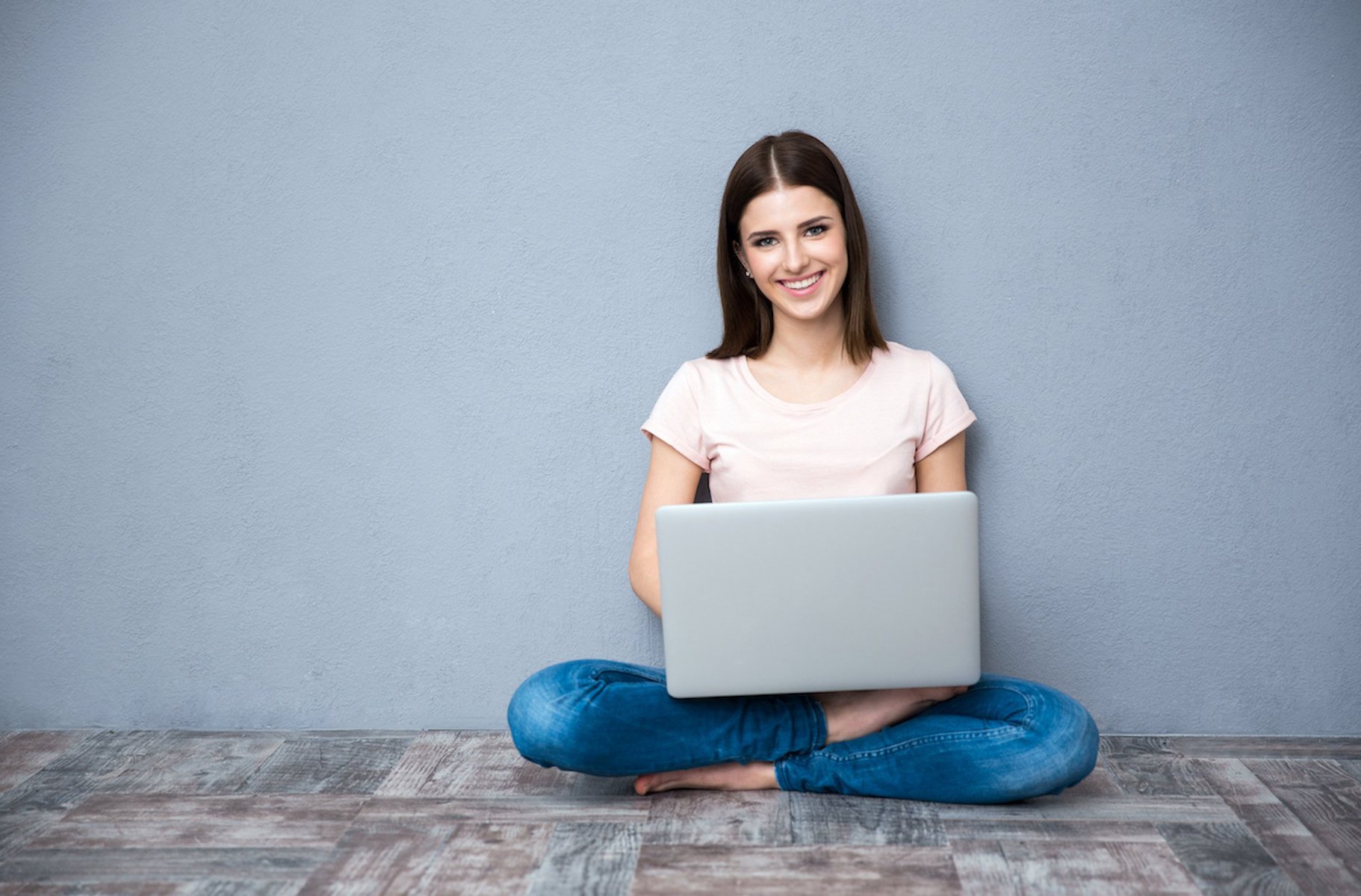 Young smiling woman sitting on the floor and using laptop